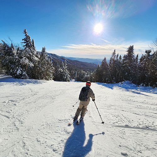 Skier moves downhill at center of ski slope under bright sun