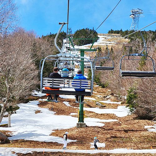 3 skiers ride a chairlift with two skiers passing underneath